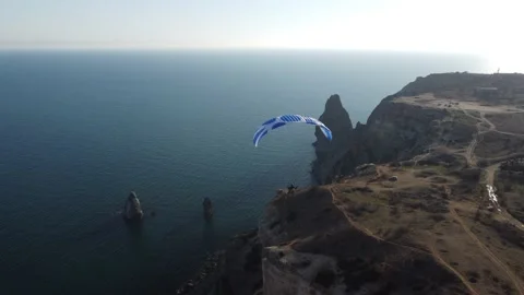 Aerial drone view of a man flying a white and blue paraglider over a hill and Stock Footage 172235517