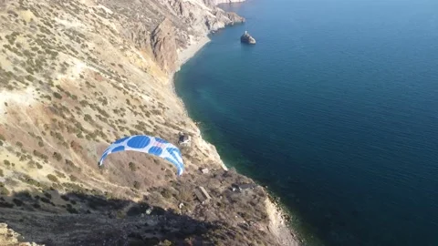 Aerial drone view of a man flying a white and blue paraglider over a hill and Stock Footage 172391797