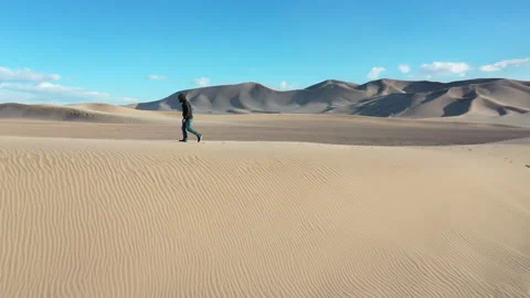 Aerial Drone View of a man walking across the top of a Sand Dune Stock Footage 326723664