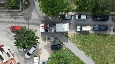 An aerial drone view of a modern garbage truck lifting a trash bin and emptying Stock Footage 276508931