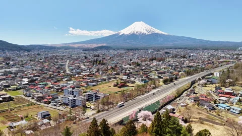 Aerial drone view of Mount Fuji rising above the town, the expressway and the Stock Footage 344992416