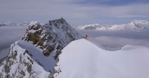 Aerial drone view of a mountain climber skier on the peak summit top of a snow c Stock Footage