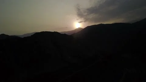 Aerial drone view moving away between dark mountains with the background sun shi Stock Footage 199564290