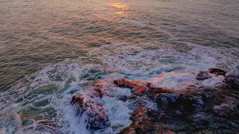 Aerial drone view of ocean waves crashing on rocky coast at sunset Stock Footage 345467080