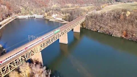 Aerial drone view of a passenger train crossing a steel railway bridge over a Stock Footage 328627841