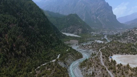 Aerial drone view of a river flowing beside dusty roads winding through Manang’s Stock Footage 311018913