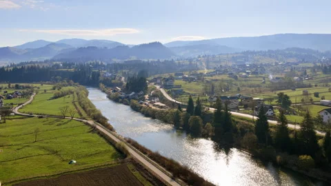 Aerial drone view of a river flowing alongside a rural road near Vatra Dornei, Видео 336302724