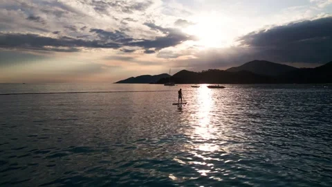 Aerial Drone View of Silhouetted Man Paddleboarding on Calm Sea at Golden Sunset Video stock 335834700