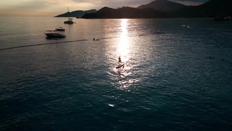 Aerial Drone View of Silhouetted Man Paddleboarding on Calm Sea at Golden Sunset Video stock 335834704