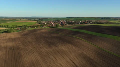 Aerial drone view of a small Czech village nestled among vast rolling plowed Stock Footage 336611576