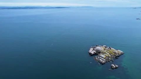 Aerial drone view of a small rocky island surrounded by calm blue ocean water Video stock 335762873