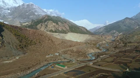 Aerial drone view of snow-draped mountains rising behind Manang’s winding Stock Footage 311019044