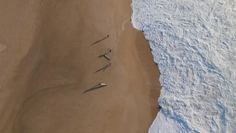 Aerial drone view of three surfers with longboards at beach in Nazare, Portugal Stock Footage 295851755