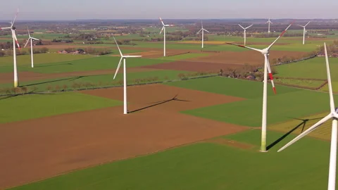 An aerial drone view tracking across multiple large wind turbines casting long Stock Footage 336460085