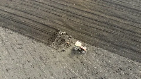 Aerial drone view of a tractor harrowing a chernozem field. Taken in the spring Stock Footage 130250159