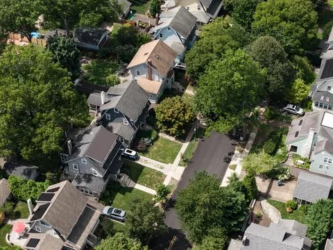 Aerial drone view of tree-lined suburban intersection, nearby homes, and local 스톡 사진