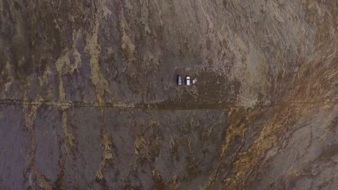 Aerial drone view of vehicles on mountain road through barren terrain, Iceland H Stock Footage 341606132