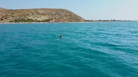Aerial drone view of a young alone girl floating in the transparent sea Stock Footage 129380428