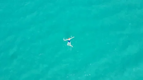 Aerial drone view of a young alone girl floating in the turquoise sea Stock Footage 129380472