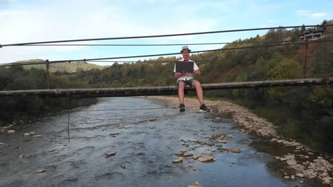 Aerial drone view of young man in white shirt sitting on wooden bridge over Stock Footage 156714802
