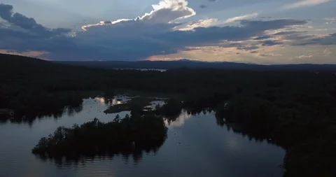 Aerial dusky puffy clouds over rippling reflective New England lake in summer Stock Footage 111523456