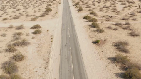 Aerial of empty paved road surrounded by sandy dirt small bushes sunny day Stock Footage 211238286