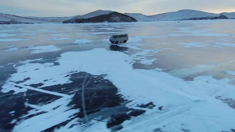 Aerial endless ice field winter lake Baikal off-road vehicle bus rides at sunset Stock Footage 165216812