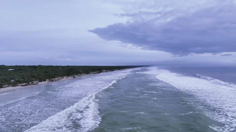 Aerial flies parallel to Rainbow Beach on a gloomy misty day as waves crash and Stock Footage 323785261