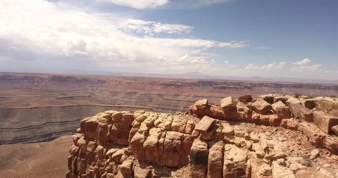 Aerial: flight along cliff ridge with goosenecks and monument valley beyond Stock Footage 99453085