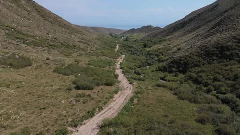 Aerial flight along a winding dirt road in a mountain valley, Kyrgyzstan Видео 347239953