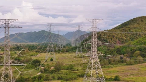 Aerial flight forward between high voltage power lines crossing a lush green Stock Footage 314973842