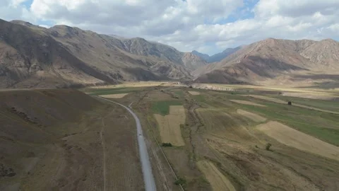 Aerial flight over patchwork fields toward rugged mountains, Kyrgyzstan Stock Footage 347241874