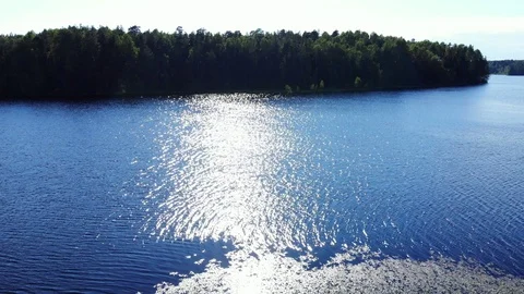 Aerial flight over sunlit dark blue lake and forest Stock Footage 92235391