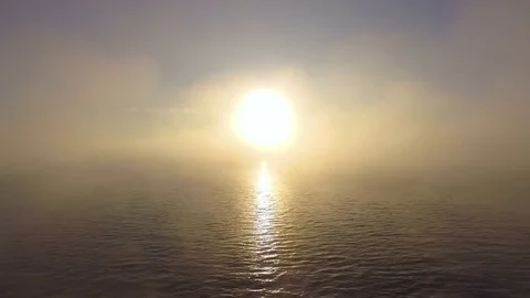 AERIAL: Flight through the mist to bright sun above the water. Stock Footage
