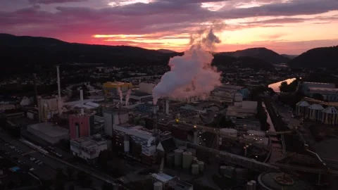 Aerial flight toward a paper mill with pink steam plume at sunrise, Austria 動画素材 344658436