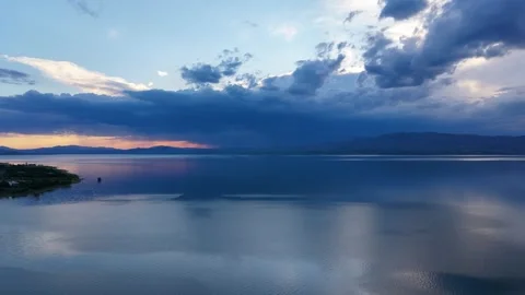 Aerial Flight Toward Sunset and Rain Clouds Over Reflective Blue Lake Stock Footage 345034910