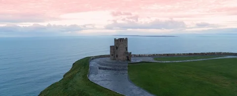 Aerial fly-by of old watchtower at the Cliffs of Moher. Red, orange sky. Mighty Stock Footage 127923856
