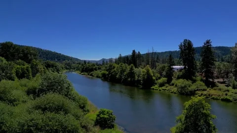 Aerial fly over view of blue water river with bright green grass and trees Stock Footage 248664110