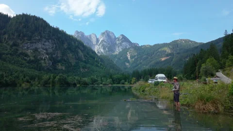 Aerial fly-by shot over man fly fishing in alpine lake, Gosaukamm background Stock Footage 331602003