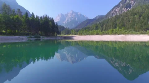 AERIAL: Flying above beautiful green lake towards the rocky mountains Stock Footage