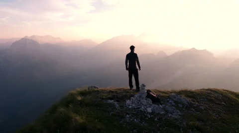 Aerial - Flying around young man standing victoriously on top of the mountain Stock Footage 65304629