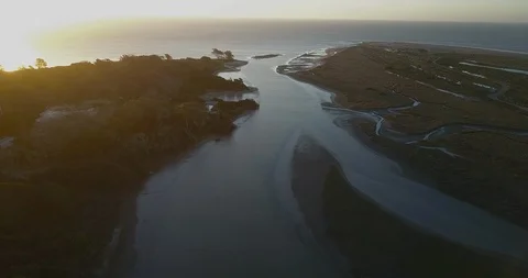 Aerial - Flying backwards over a river that ends on the sea on sunset Stock Footage 85645582