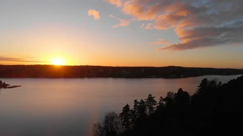 Aerial flying forward from forest trees toward archipelago water colorful sunset Stock Footage 104525808