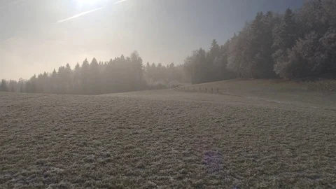 AERIAL: Flying low over frozen icy fields wrapped in fog on sunny winter morning Stock Footage