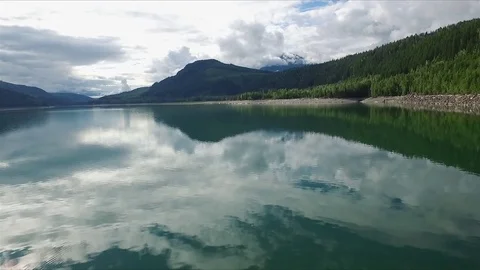 Aerial flying low over large blue green mountain lake with pan up Stock Footage 75448426