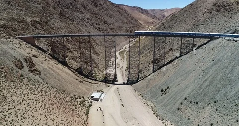 Aerial flying over train while it drives through old bridge at desertic mountain 스톡 동영상 107220430