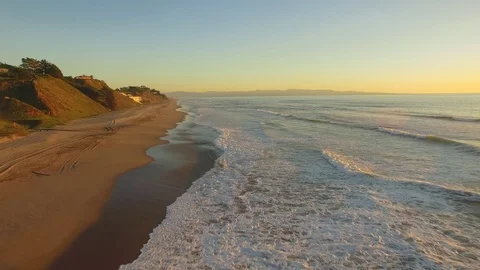 Aerial flying shot down a beach in California over the sand and water. Video stock 88423660