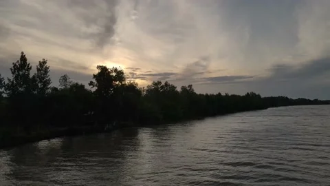 Aerial flyover cloudy sunset at river with sun behind trees Stock Footage 151701112