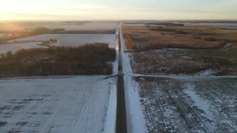 Aerial flyover of empty road between frozen, snowy farmland and fields. 库存影片 157768551