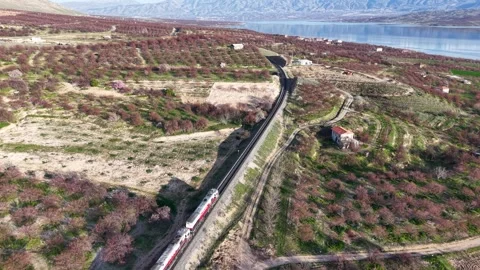Aerial Follow of Freight Train Toward Lake and Snowy Mountains Stock Footage 345752370
